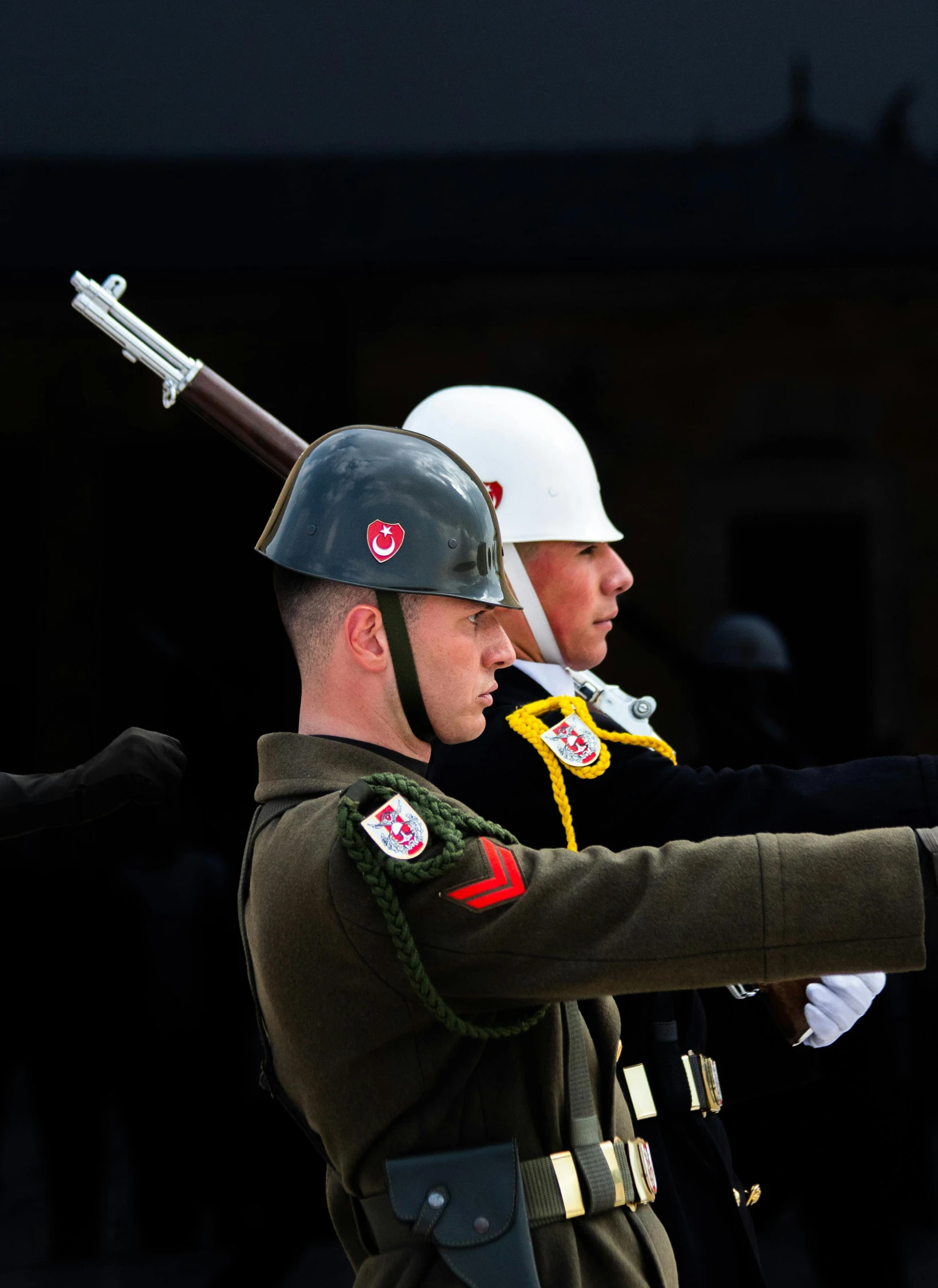 two people in uniform holding up a rifle to another person