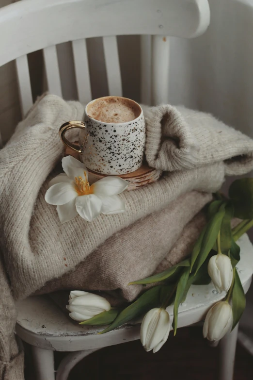 a stack of sweaters, coffee cup and flowers on top of a chair