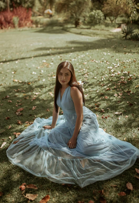 a woman is sitting on the grass, in a long dress