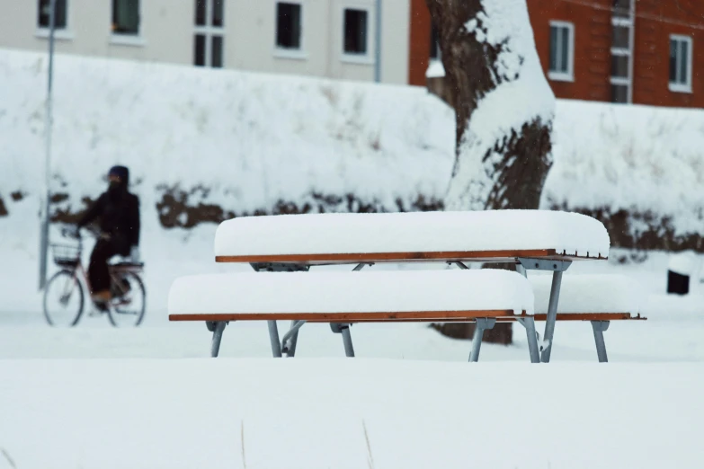 a bench is covered with white snow in front of buildings