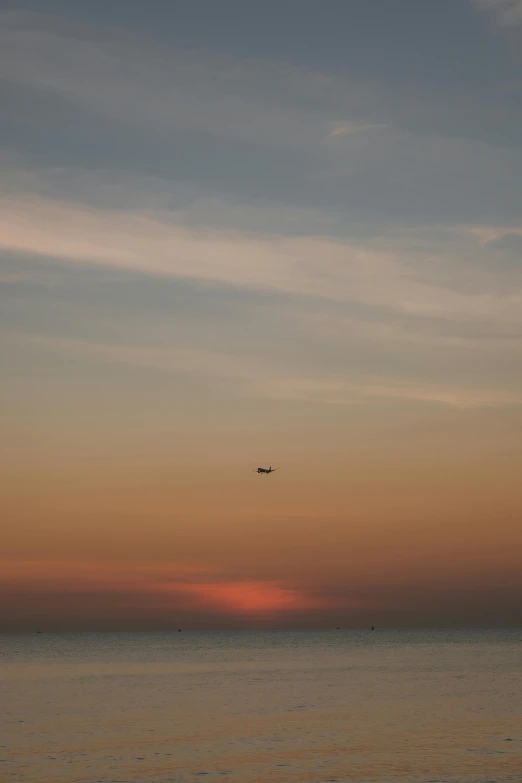 a jet plane flying over the ocean at sunset