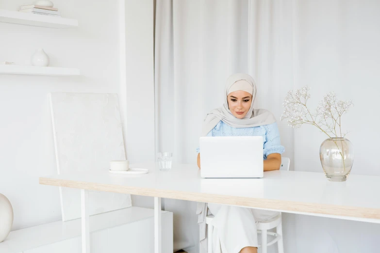 a woman is sitting at a white desk with a laptop