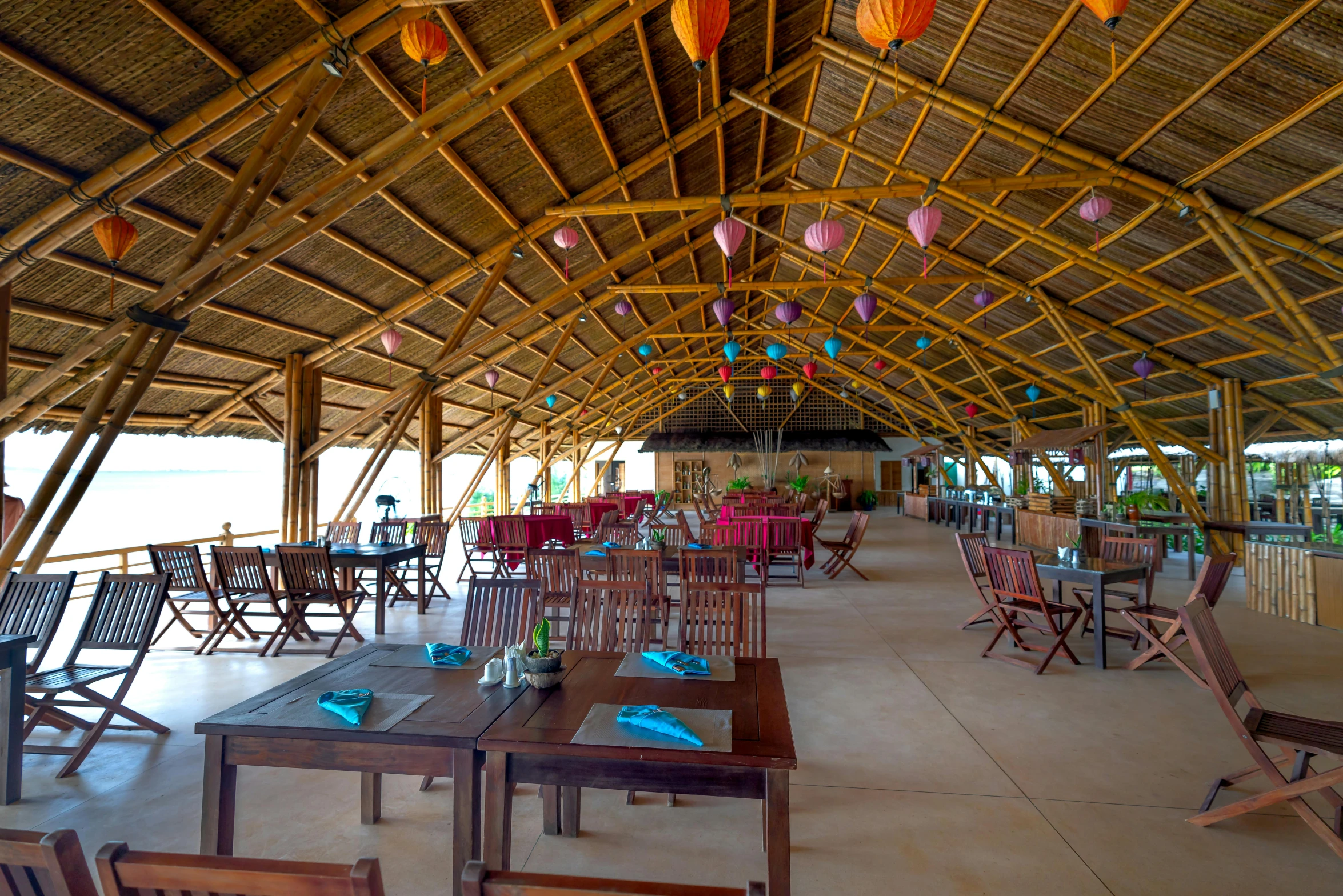 a long dining hall has a ceiling full of brightly colored hanging lanterns