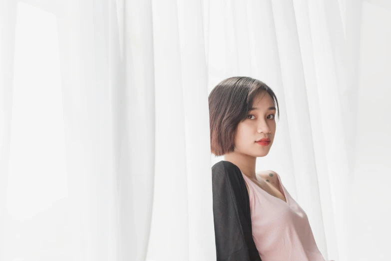 a woman stands in front of curtain while wearing a pink top