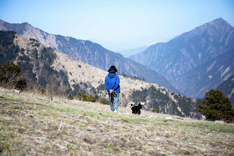 a woman with a dog standing on top of a grass covered hill