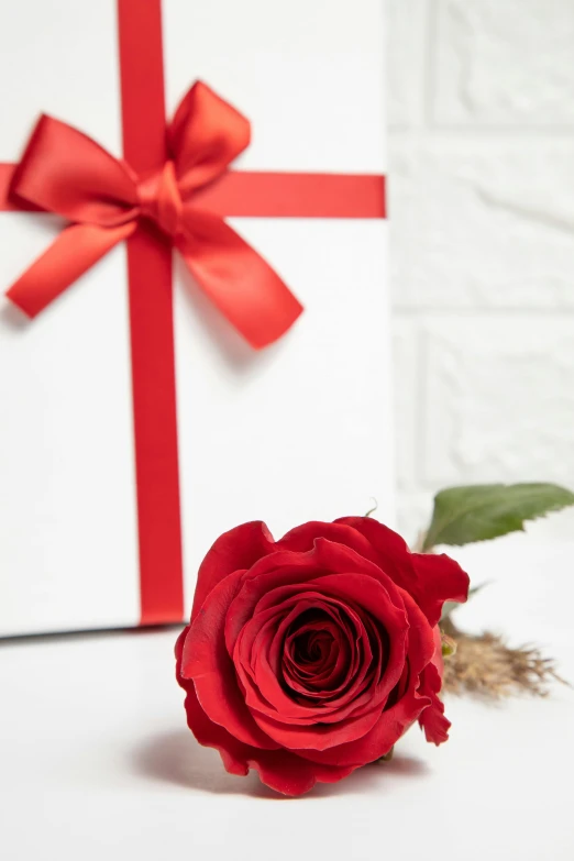 a red rose is next to a gift with the ribbon tied