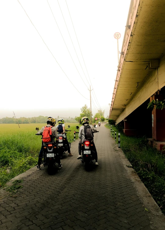 three people riding motorcycles on the road by a bridge