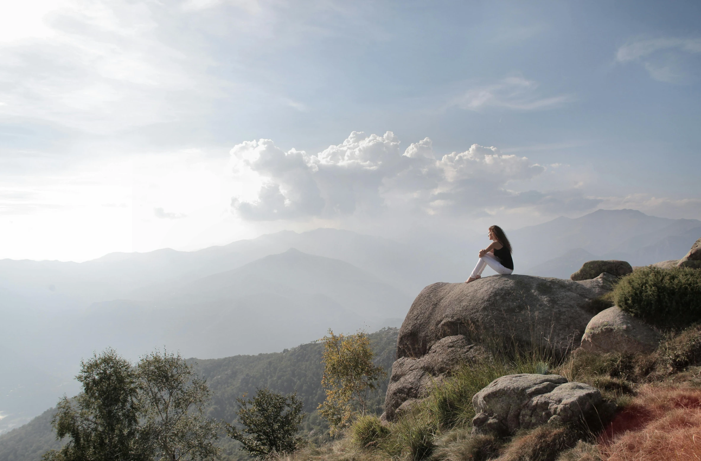 a woman sits on top of a mountain with a valley in the background