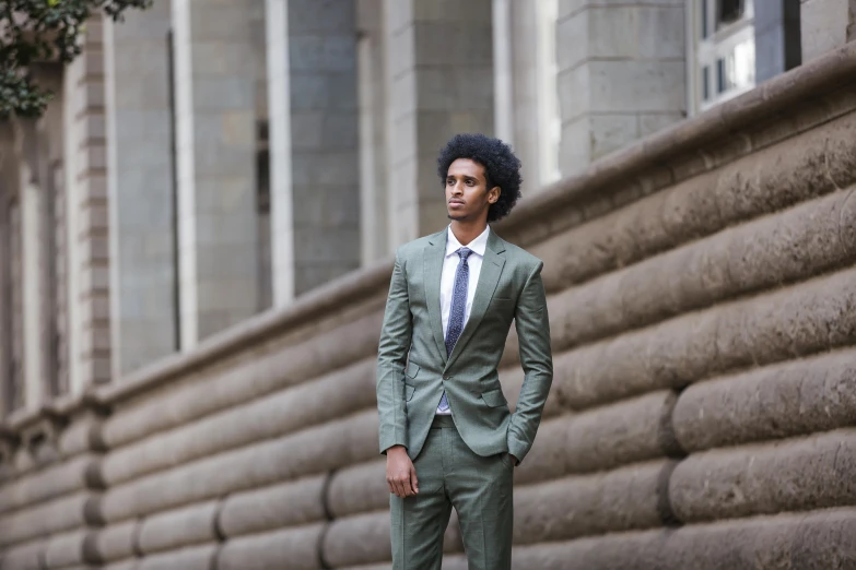 a man in a green suit and tie standing in front of a building