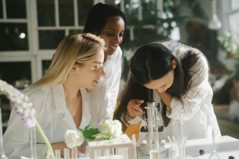 three women in white are examining an object on a desk