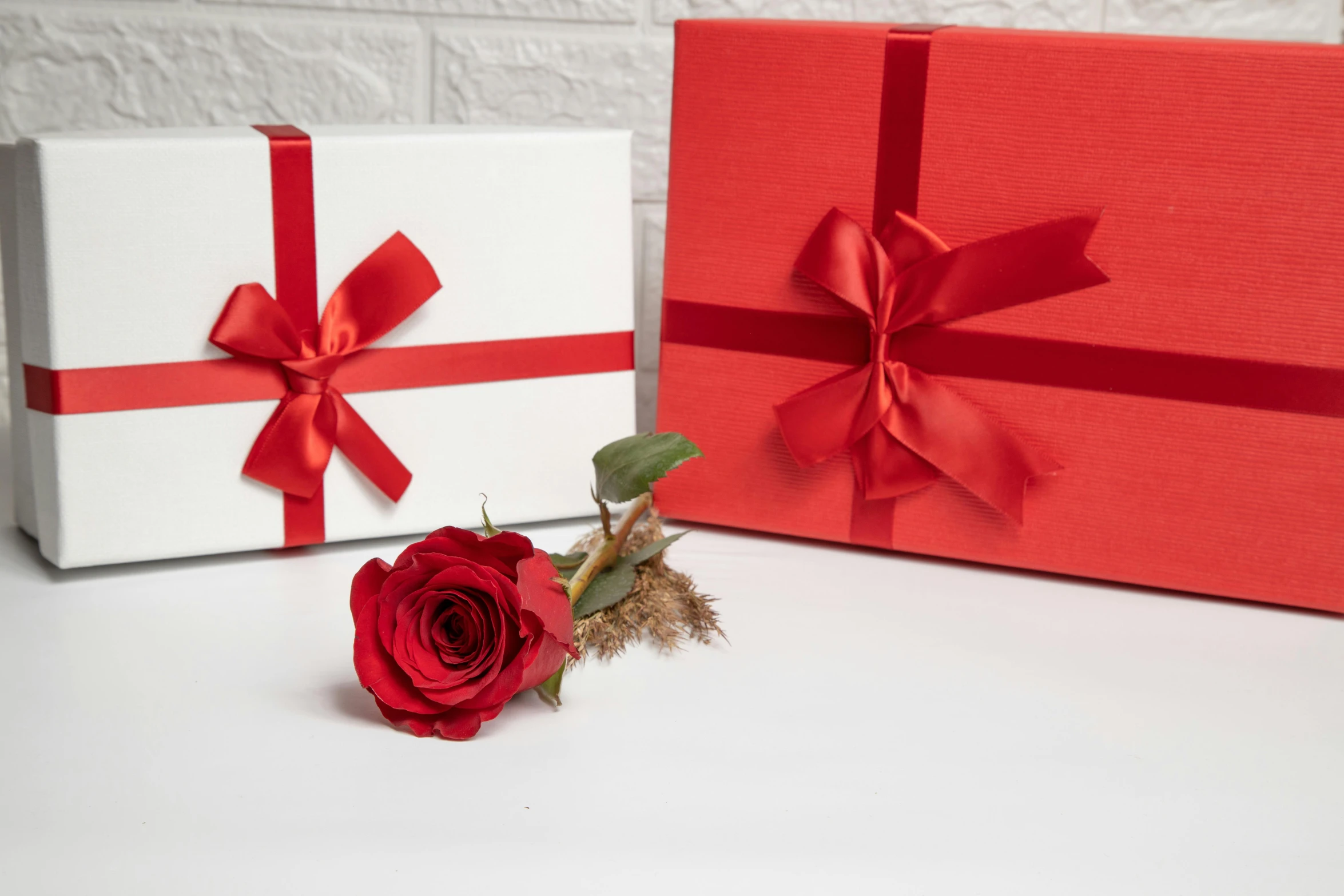 an orange rose next to two large white gift boxes