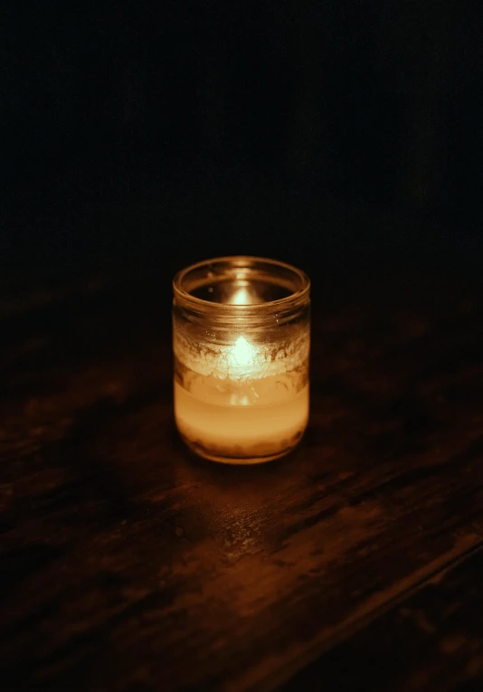 lit candle inside glass with wooden table