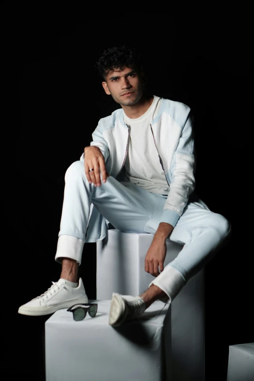 a man sitting on a cube wearing a jacket and jeans