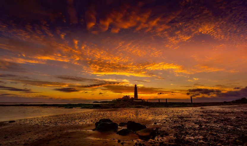 an orange and red sunset in a beach with a lighthouse in the distance