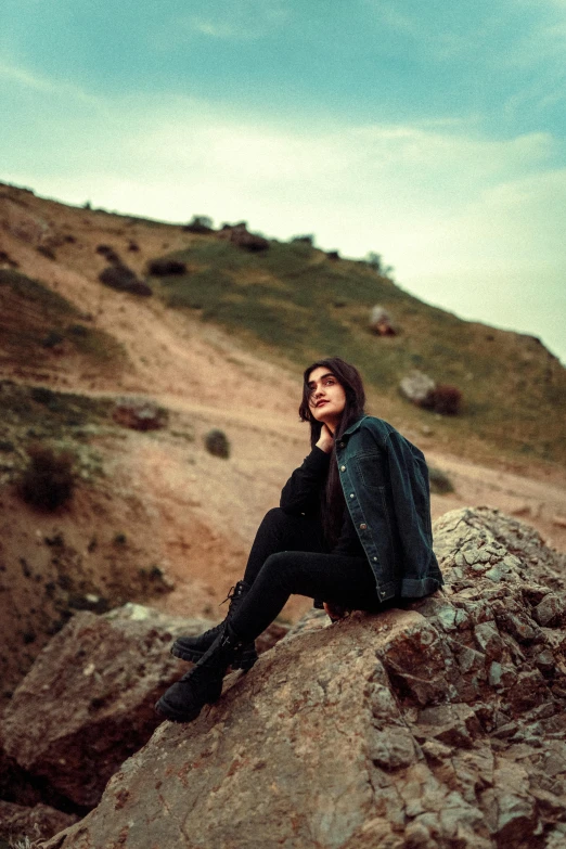 a woman sits on top of a rock while looking off into the distance