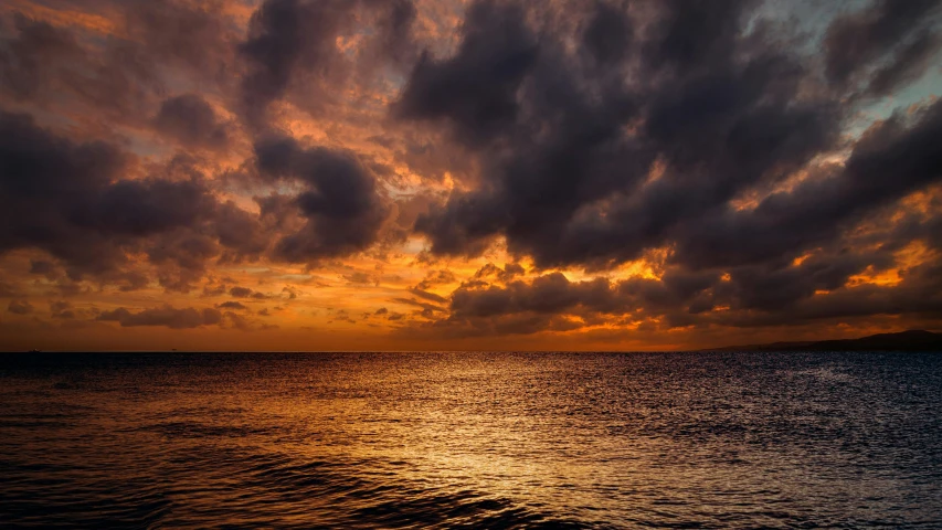 an orange sunset is over the ocean and there are clouds in the sky