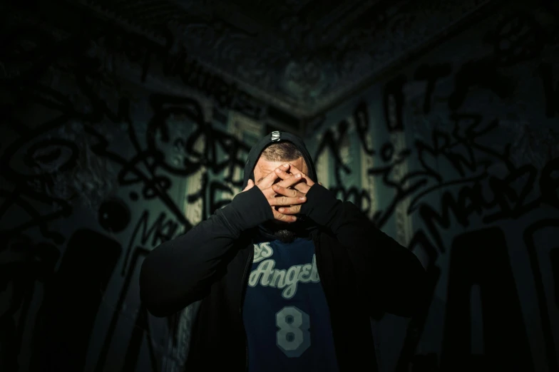 a man in a jacket covering his face in front of graffiti