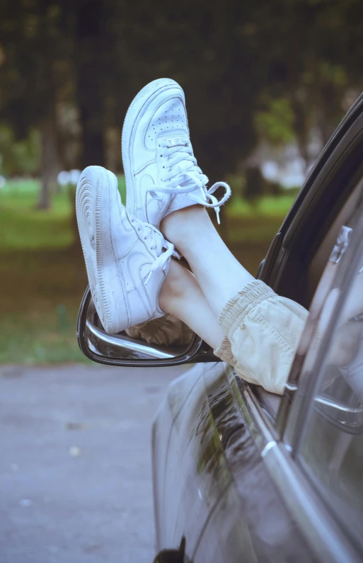 the feet of a woman wearing tennis shoes hanging out of a car door window