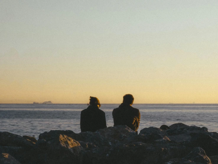 two people are sitting on rocks near the ocean