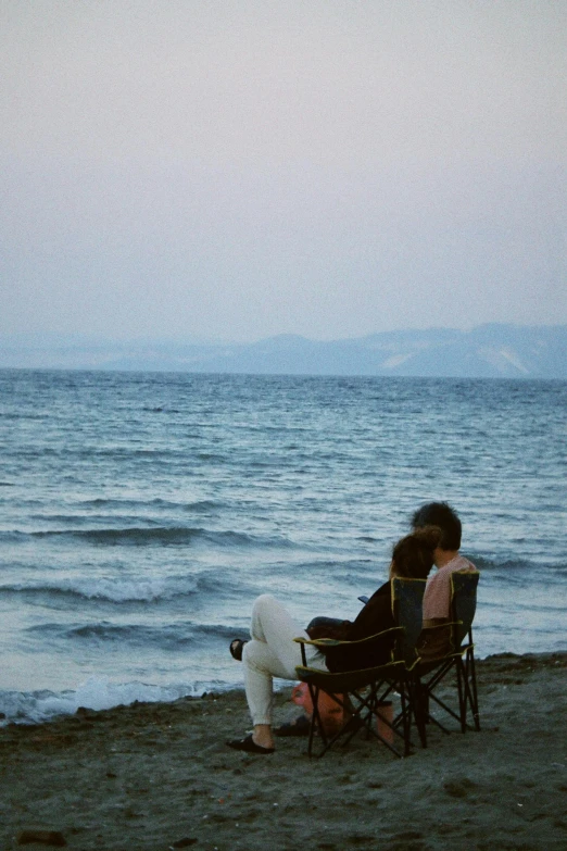 two people sitting on top of chairs facing the water