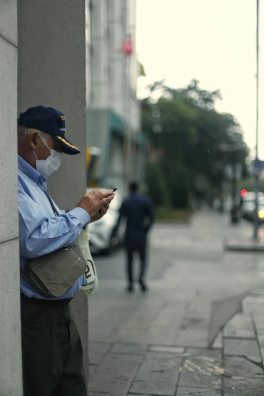 an older man wearing a surgical mask and looking at his phone on the sidewalk