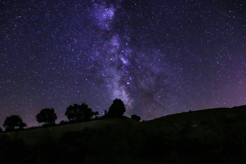 a very beautiful night sky filled with stars and some trees