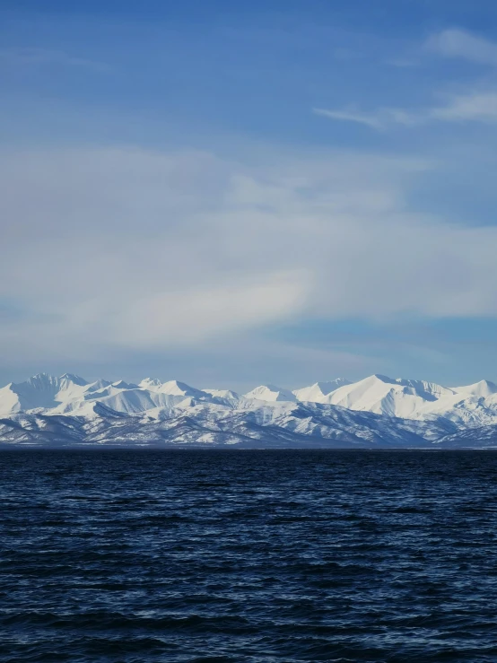 mountain range in background from calm water with white capped peaks