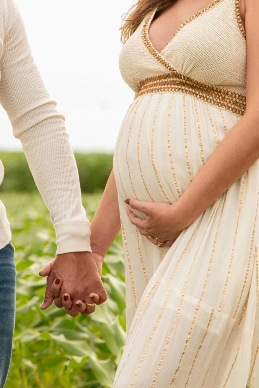 a pregnant woman holding hands with a man in a field