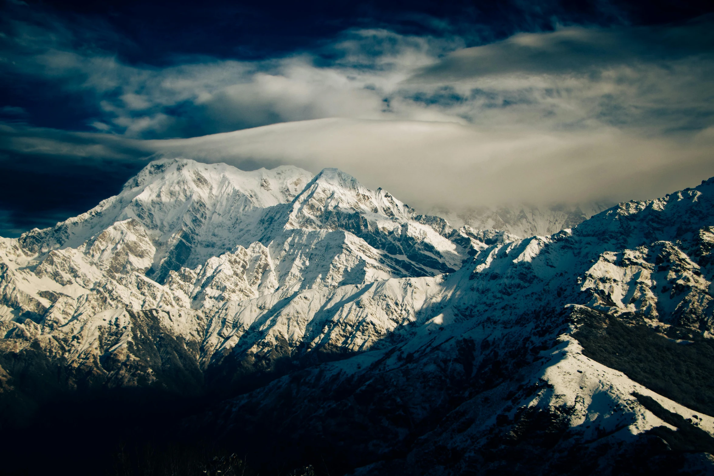 clouds gather over the top of snowy mountains