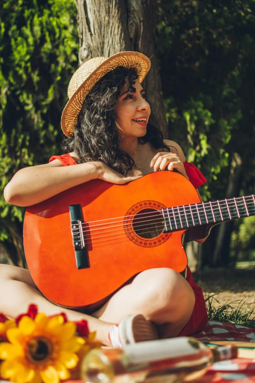 a woman sits under a tree, holding an orange guitar