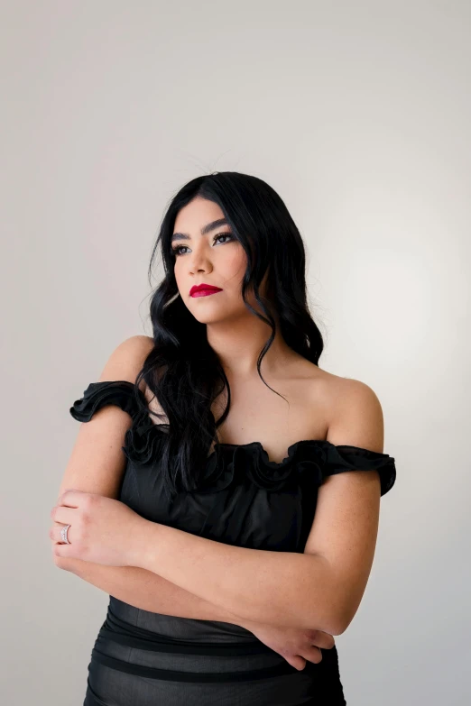 a woman posing with her arms crossed wearing a black dress