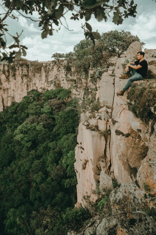 a man with his legs crossed and sitting on a cliff ledge