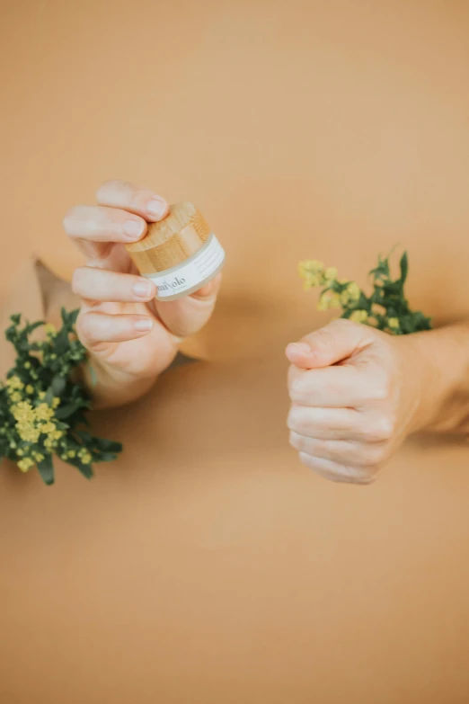 a close up of two hands holding a small jar of cream