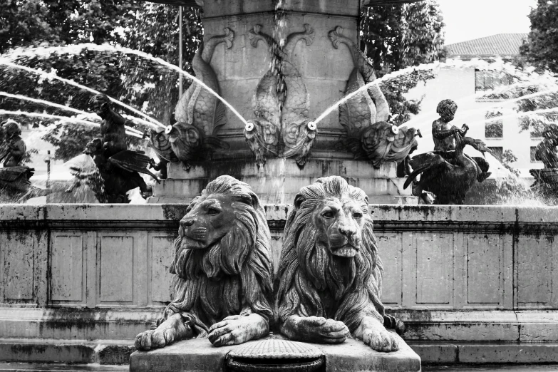 the statue of lion heads is beside the fountain with water shooting from it