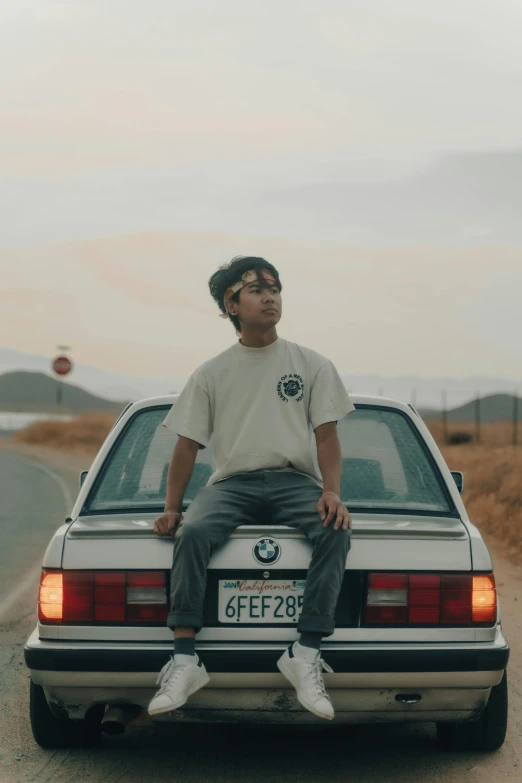 a man sitting on the hood of a car while standing beside it