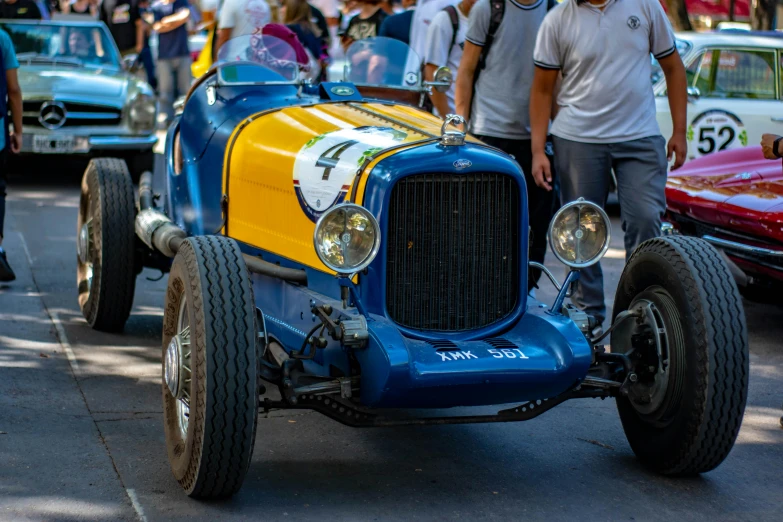 an older model t race car with lots of people walking