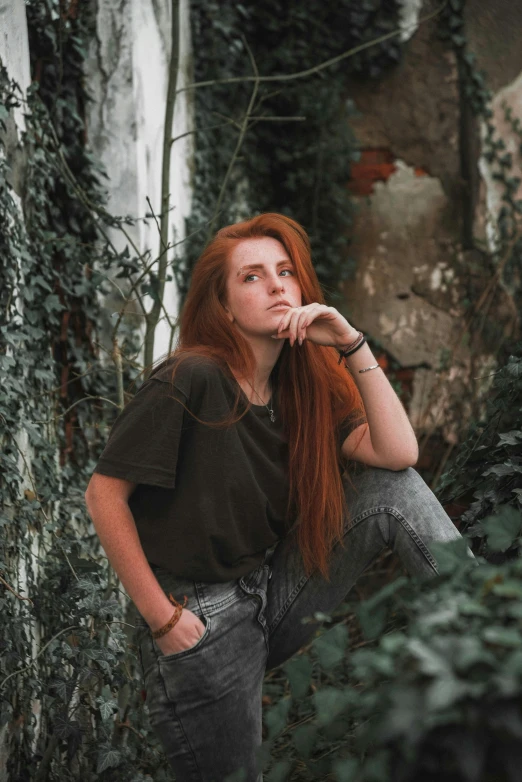 a red - headed woman leans her head on a ledge in front of foliage