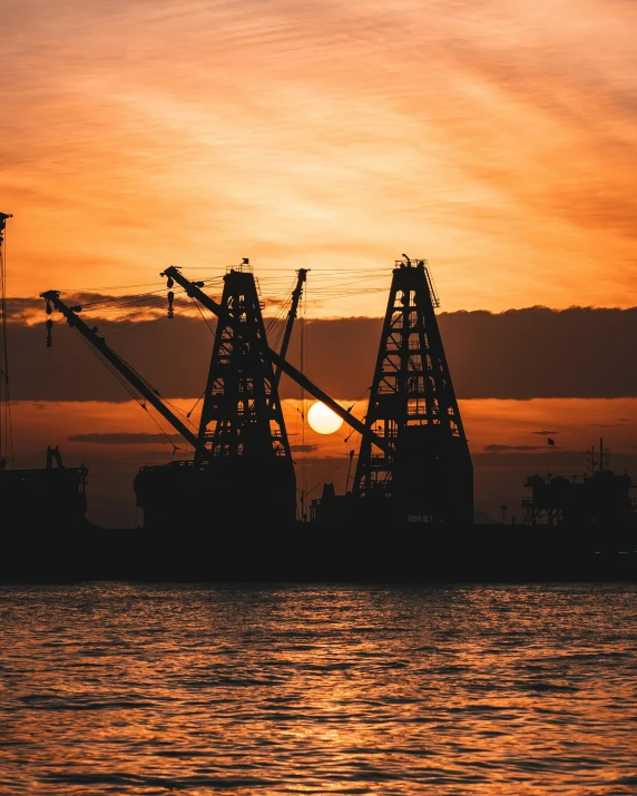 the silhouette of two cranes on a sunset