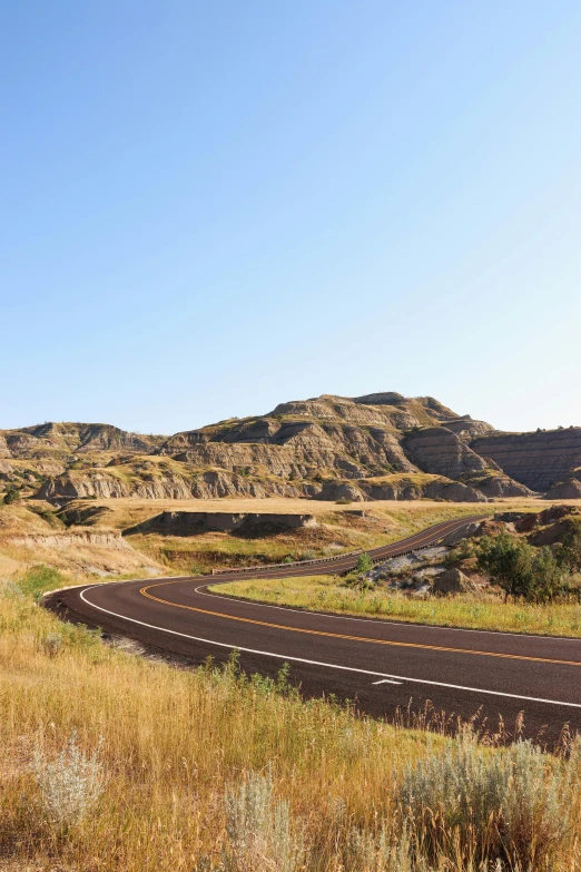 a lonely road winding through a field with tall grass and hills in the background