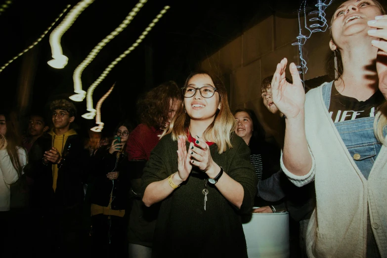 two woman standing and clapping in the crowd with lights in the background