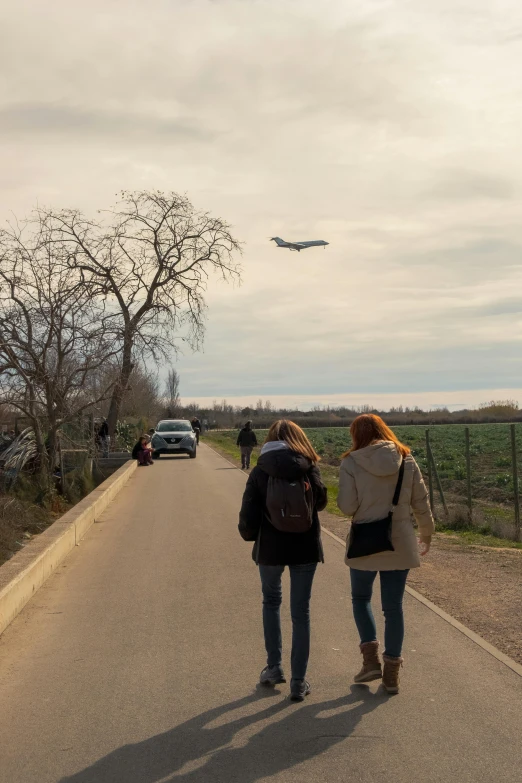 two people standing in the street, watching an airplane
