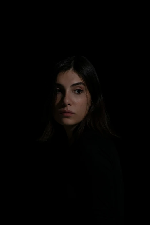 woman standing alone against a dark background with dark hair