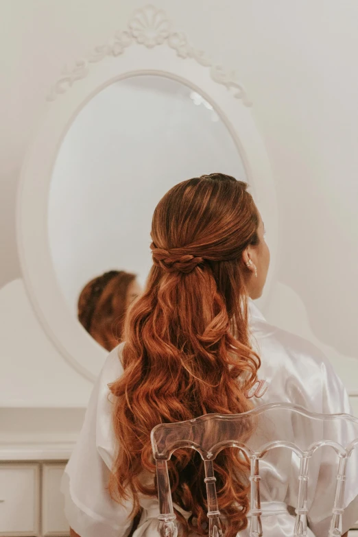 bride in bridal gown sits behind the hair dresser looking into her mirror