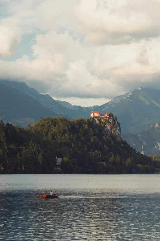 a boat floats along the still water surface as clouds loom over a mountain