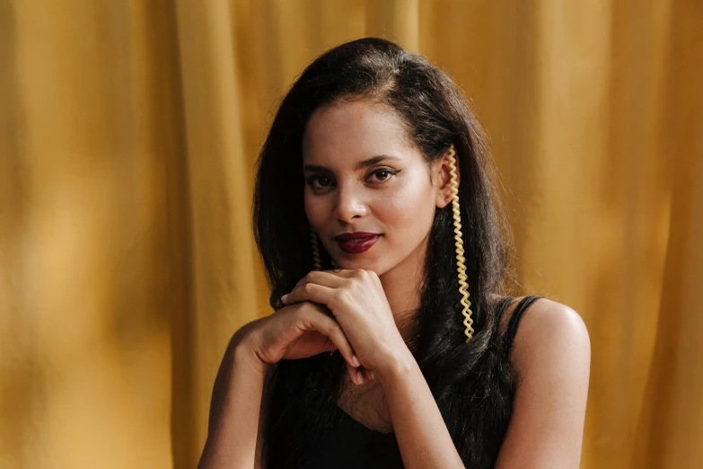 a woman wearing large, dark blue earrings sitting in front of a yellow curtain