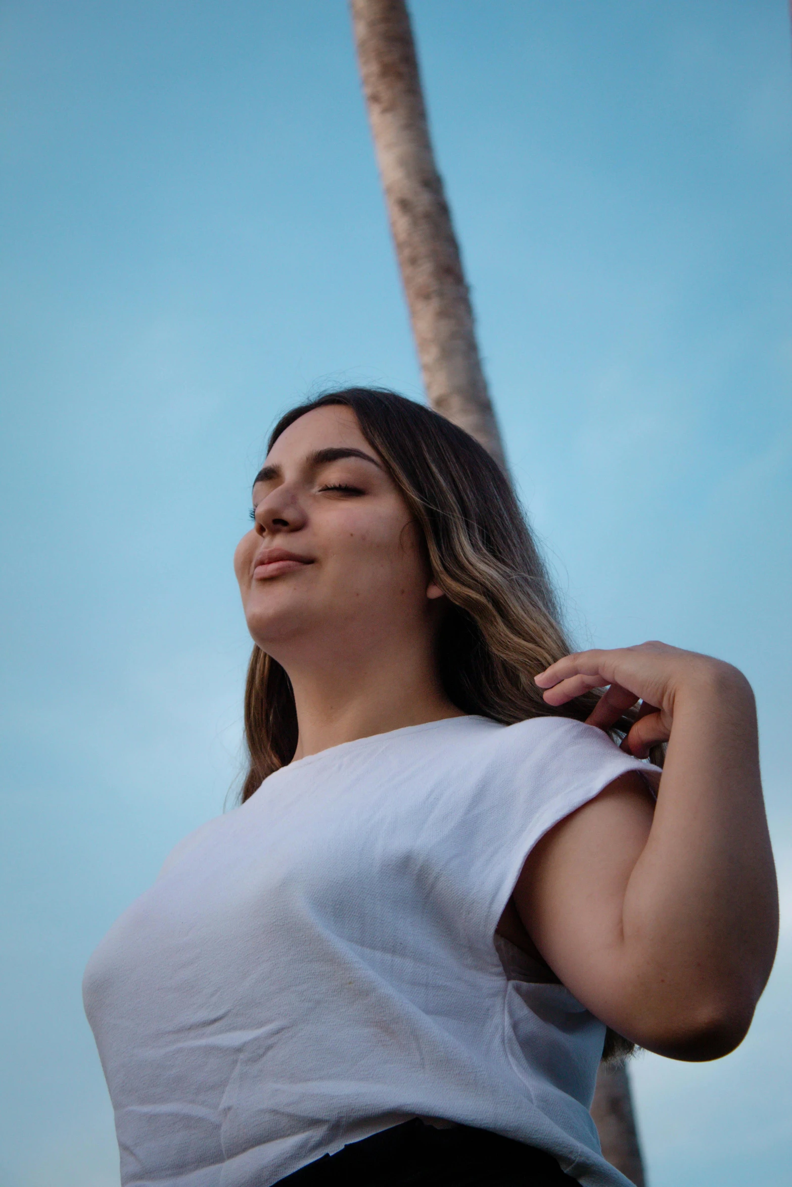 a young woman stands next to a palm tree