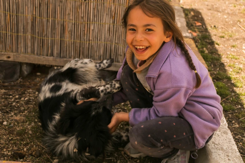 a girl pets a goat while a dog lies next to her