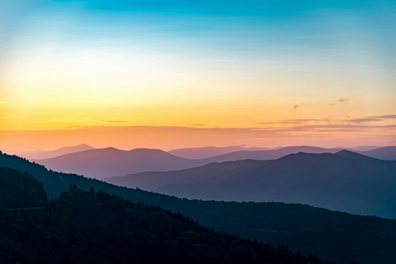 sunrise over mountains with trees and clouds in the foreground