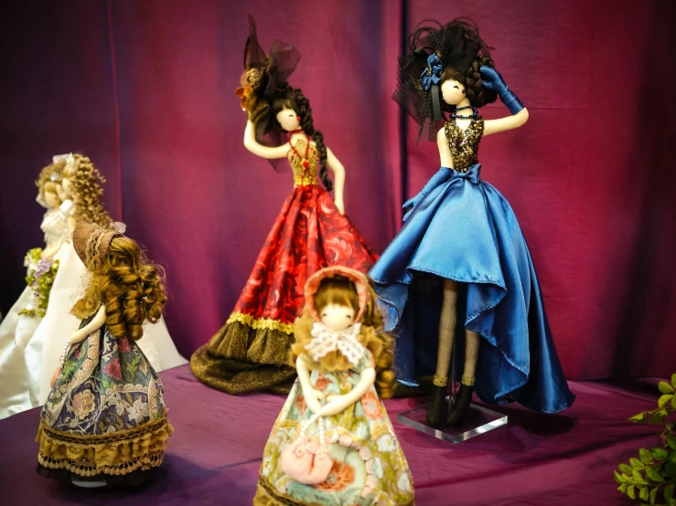 three porcelain dolls in dresses and accessories on a purple surface