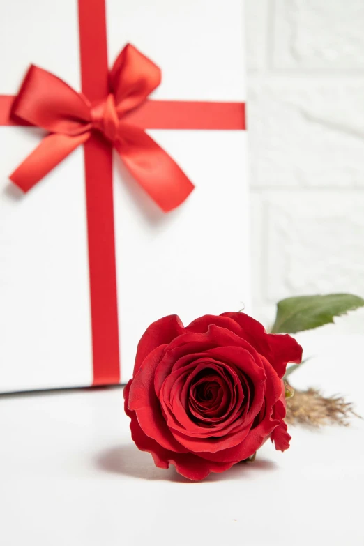 a single rose in a paper vase sitting in front of a large white gift box